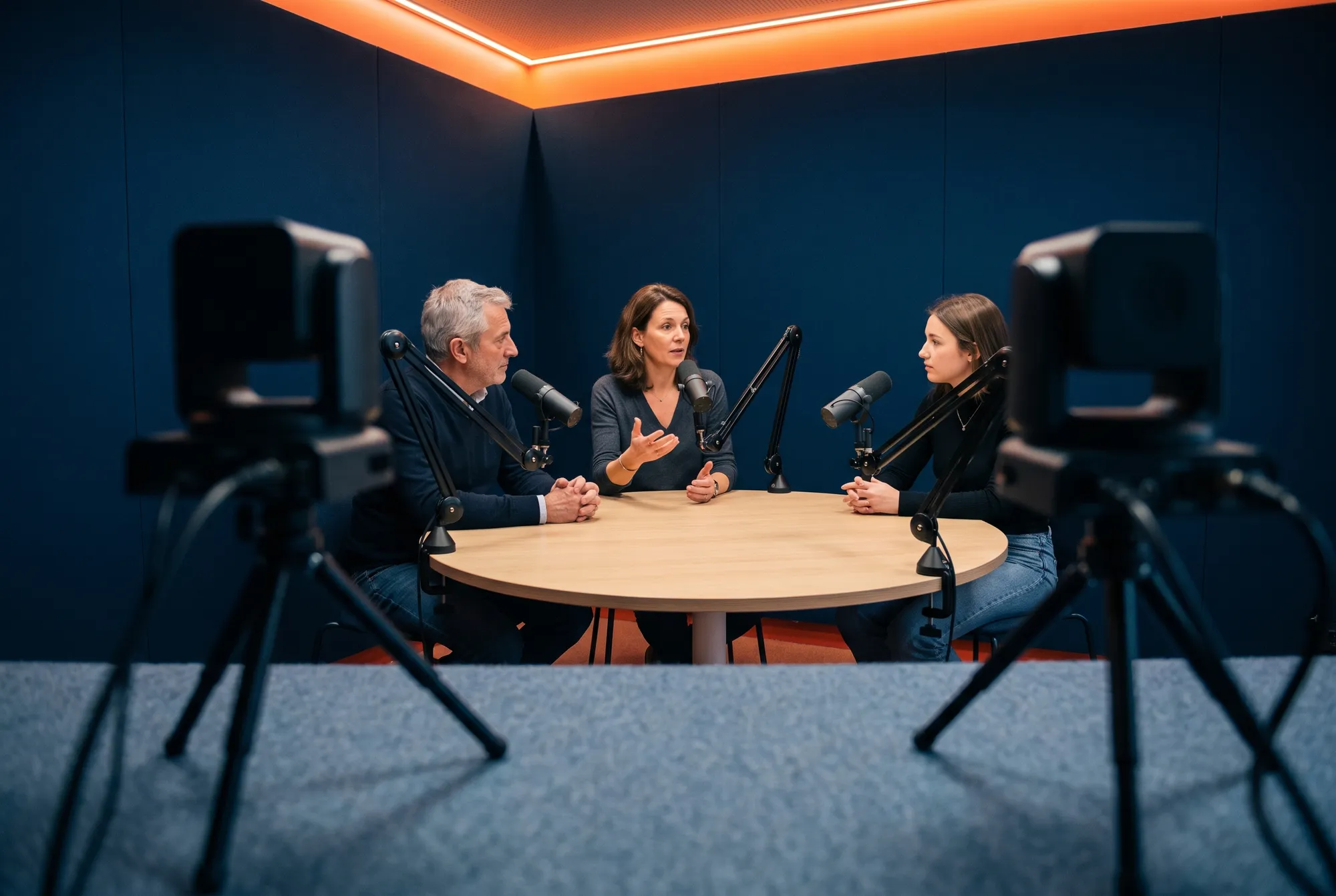 Podcast long format vu de derrière deux caméras PTZ : trois intervenants échangent autour d'une table ronde en bois
