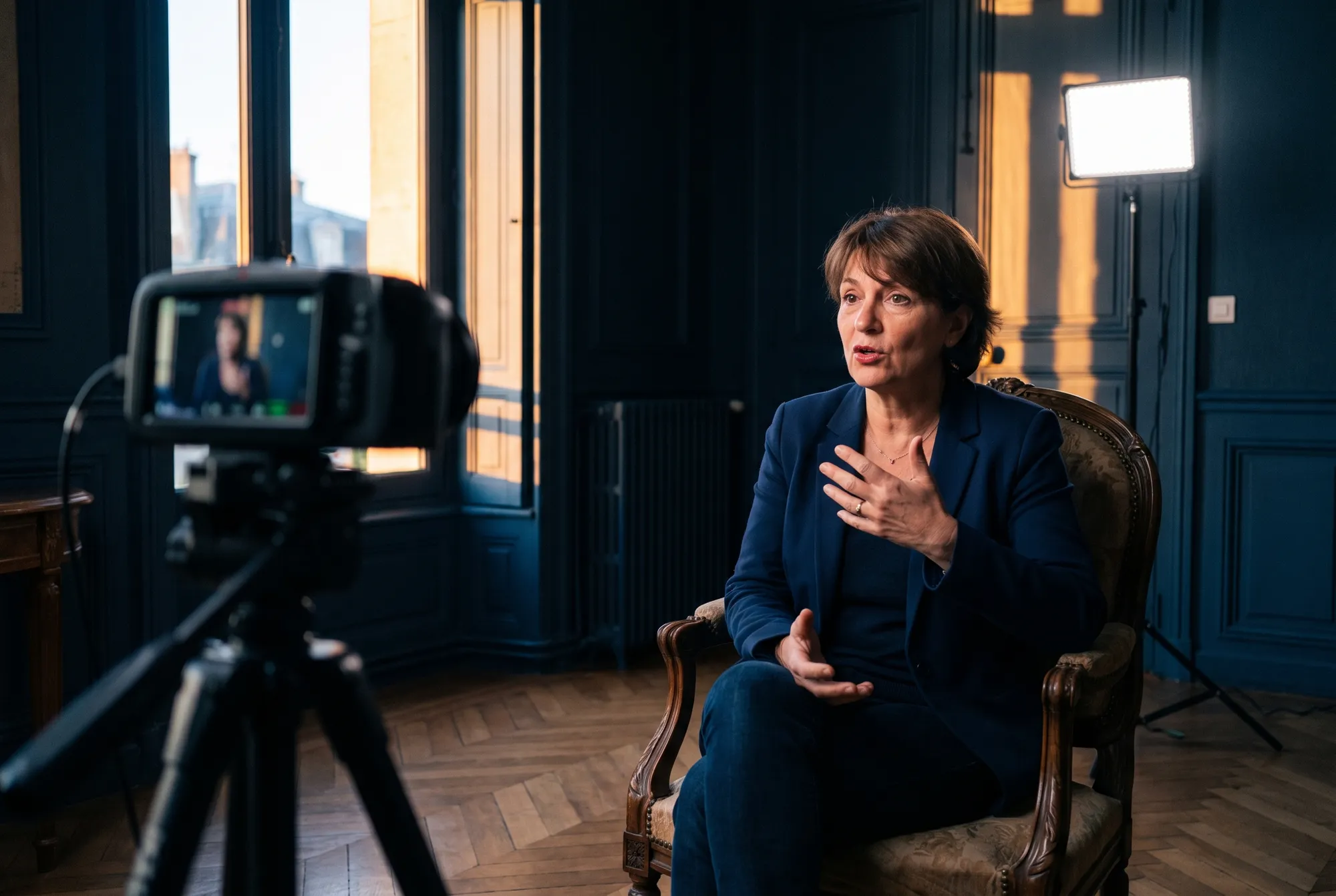 Tournage de l’interview d’une élue assise dans un bureau de mairie boisé, caméra sur trépied et panneau LED allumé