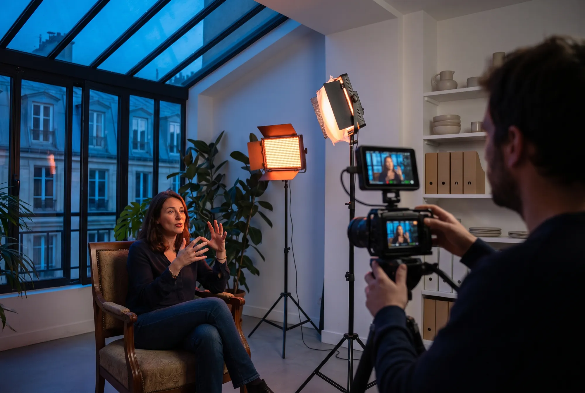 Interview d’une dirigeante d’agence dans un atelier à verrière, éclairée par des panneaux LED et cadrée par une caméra sur trépied