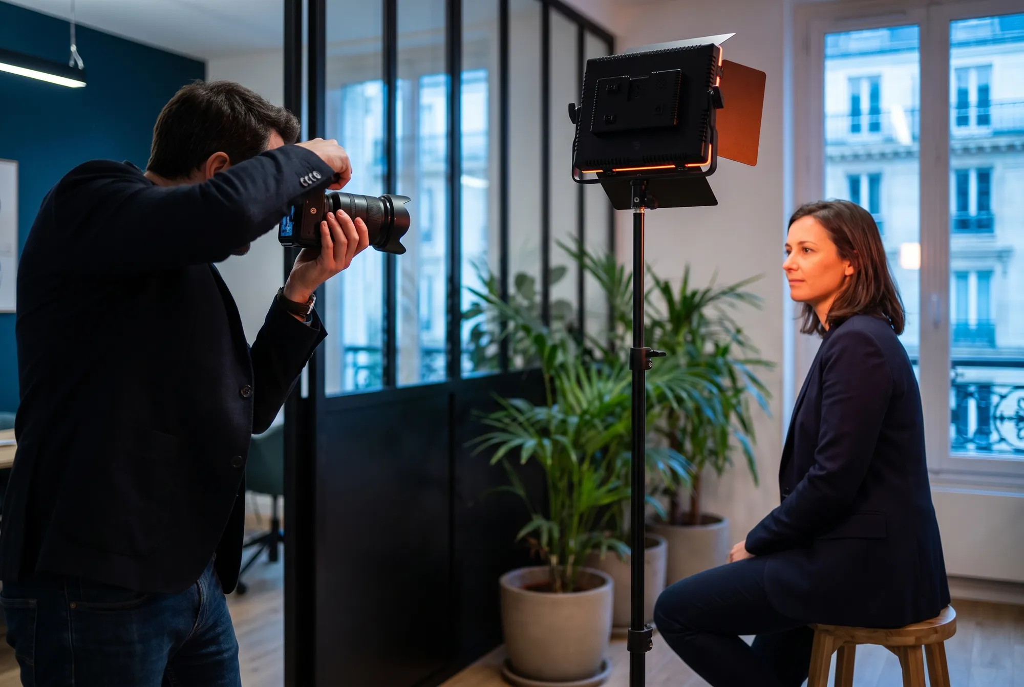 Séance photo corporate dans un bureau parisien : un photographe cadre une consultante assise près d’un panneau LED