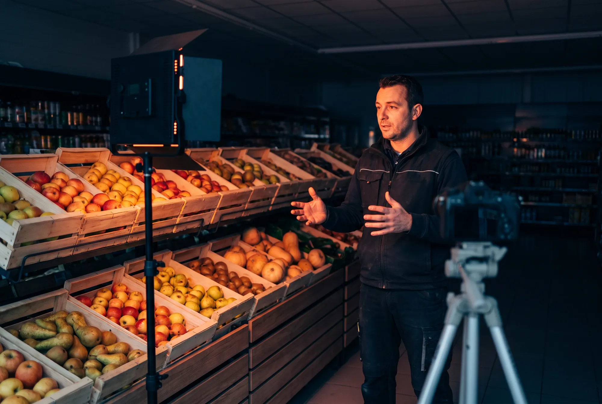 Interview d’un chef de rayon devant les cagettes de fruits et légumes d’un supermarché avant l’ouverture, éclairé par un panneau LED